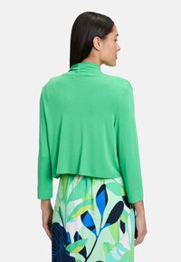 Haut vert léger et court avec des manches longues et un col montant, associé à une jupe à motifs présentant des motifs de feuilles bleu et vert.