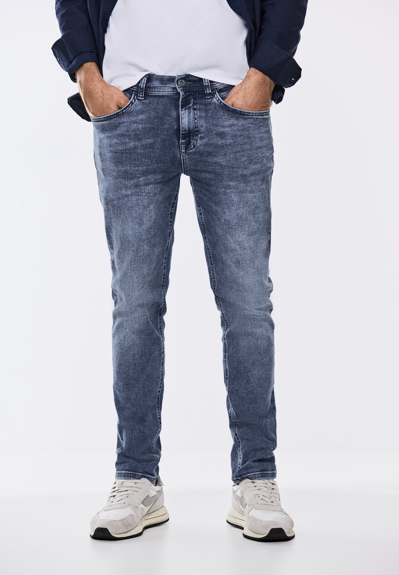 Bleka blå skinny jeans med en slät yta, fem fickor och knäppning, i kombination med ljusa sneakers.