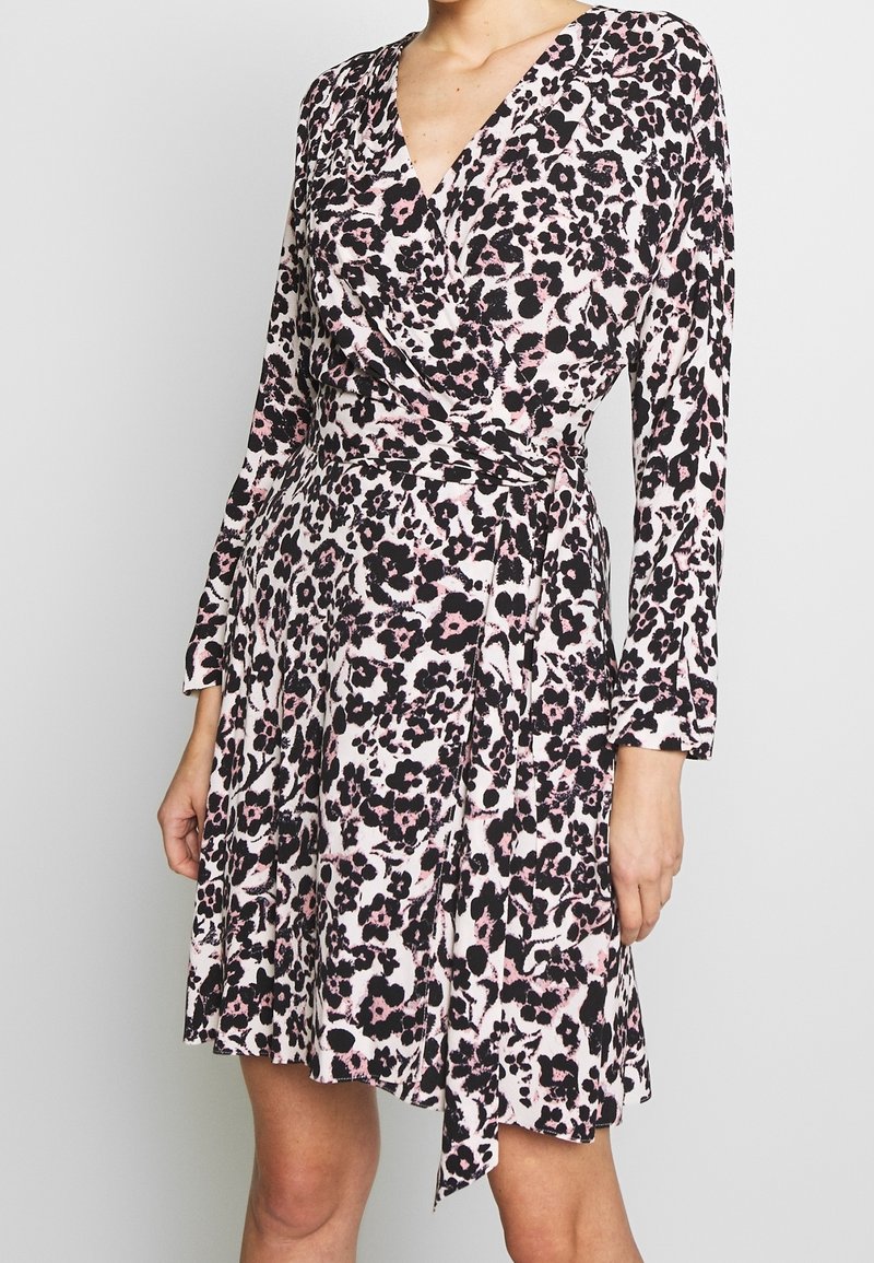 Femme portant une robe portefeuille mi-longue à manches longues avec un motif abstrait de léopard rose, noir et blanc.