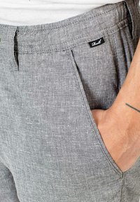 Gray linen trousers feature a textured fabric, front pockets, and a visible brand label near the waistband. The fit is relaxed.