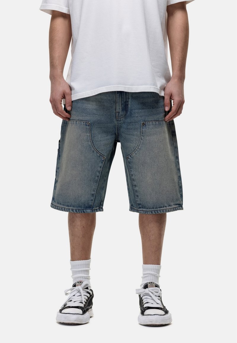 Jasnoniebieskie szorty dżinsowe, luźny krój z bocznymi kieszeniami, wykończone surowymi brzegami. Połączone z prostą białą koszulką i czarnymi sneakersami.