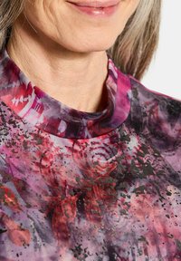 Korte mouw top met een getextureerd, multicolor ontwerp in paars, rood en zwart, met een hoge kraag en artistieke patronen.