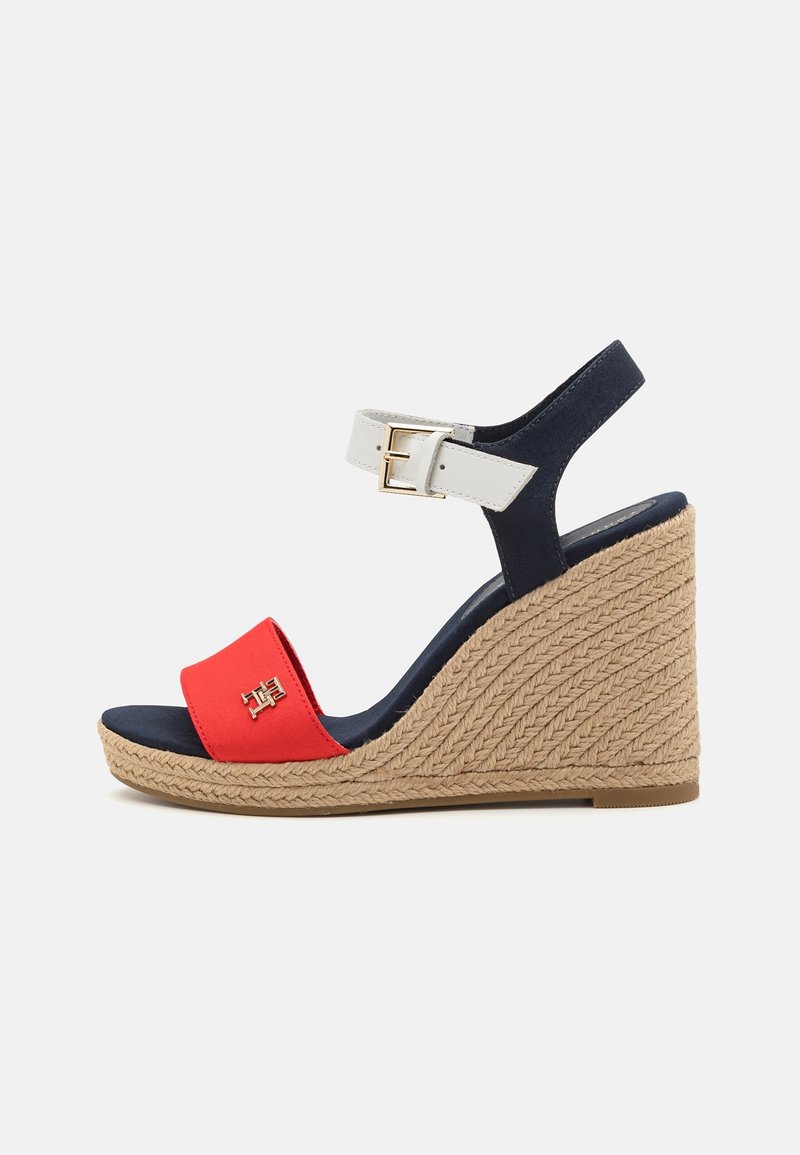 Sandale compensée avec talon en jute tressé, semelle marine, bride rouge à l'avant avec logo, et bride blanche réglable à la cheville avec boucle dorée.
