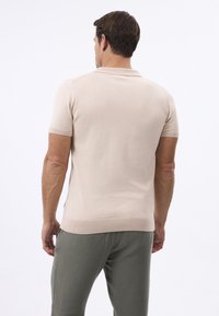 Polo shirt a maniche corte di un beige chiaro con tessuto a maglia testurizzato e polsini a coste. Indossato con pantaloni verde oliva, visto da dietro.