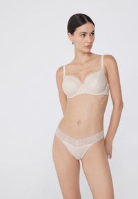 Béžový krajkový bralet s měkkými košíčky a nastavitelnými ramínky, v kombinaci s odpovídajícími kalhotkami ve stylu bikiny s vlnkovaným krajkovým pasem.