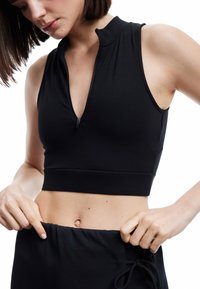 Top corto atlético negro con cierre de cremallera y cuello alto. Tela suave, diseño sin mangas, con una silueta ajustada y cintura elástica.