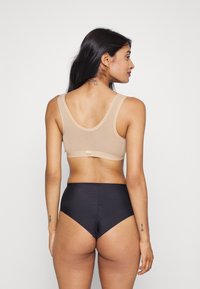 Beige nahtlösser bralette med breda band och en slät yta, kombinerad med höga svarta trosor med en glänsande finish.