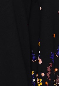 Tissu noir orné de broderies florales colorées en rose, orange, jaune et bleu. Le motif comprend diverses formes et détails de fleurs.