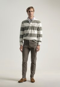 Camisa polo de manga larga a rayas en blanco y verde olivo, combinada con pantalones chinos marrón claro y mocasines de ante marrones. Diseño simple y clásico.