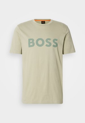 Tricou din bumbac bej, cu un logo verde proeminent "BOSS" pe față, mâneci scurte și un guler clasic de tip crew.