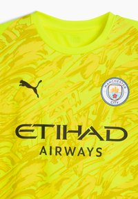 Ljusgul sporttröja med ett dynamiskt mönster. Svart Puma-logga och texten "ETIHAD AIRWAYS" med Manchester City-emblemet på bröstet.