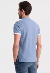 Pánská polo tričko s krátkým rukávem v světle modré barvě, s límečkem a kontrastními bílými lemy na rukávech. Vyrobeno z texturované bavlny.