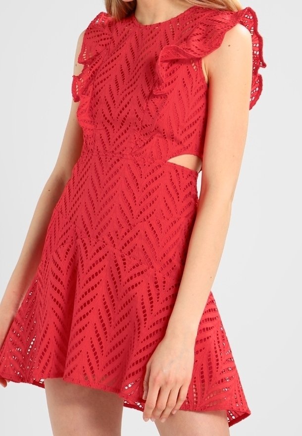 Femme portant une robe rouge en dentelle sans manches avec des détails volantés aux épaules et des découpes à la taille.