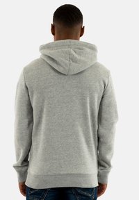 Sudadera con capucha gris, realizada en una tela suave, con un bolsillo tipo canguro, puños y dobladillo de canalé. Vista desde la parte posterior.