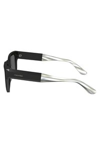 Gafas de sol con frontal de plástico negro y elegantes brazos de metal plateado con un diseño curvado. Logotipo de "Calvin Klein" en la patilla.