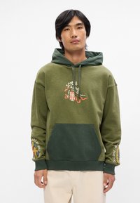 Ελιά πράσινη φούτερ με καγκουρό τσέπη, πολυεπίπεδο πράσινο καπέλο και κεντημένα γραφικά λεπτομερώς σε πορτοκαλί και μπλε στους ώμους.