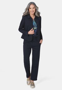 Marineblazer met een kraag, knopen aan de voorkant, gecombineerd met bijpassende broek en een patroon-top. Heeft metallic accenten op de schoenen.