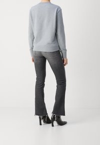 Sweat-shirt gris avec ourlet côtelé, associé à un jean foncé évasé avec ourlet effiloché et des chaussures à talons noirs, vu de l'arrière.