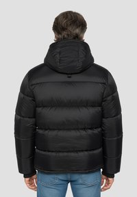 Giacca imbottita nera con cappuccio, caratterizzata da un design trapuntato e una leggera lucentezza. I polsini sono elasticizzati e il cappuccio è regolabile con un laccio.