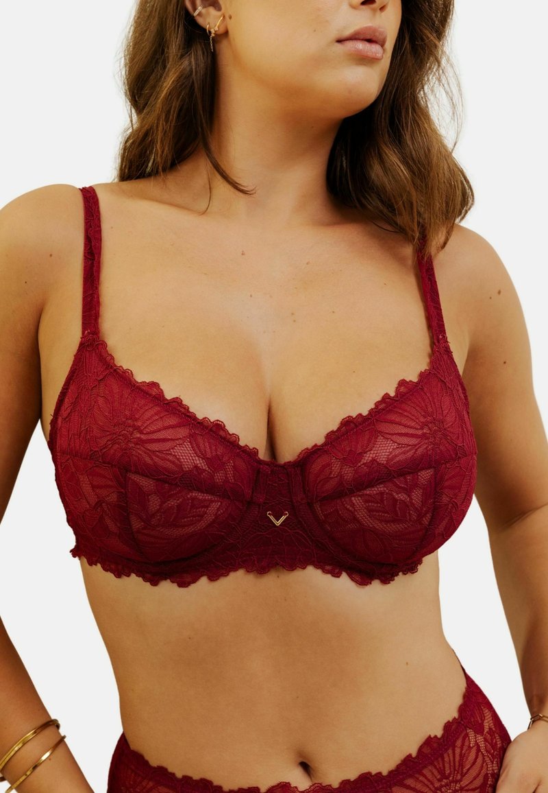 Soutien-gorge en dentelle bordeaux avec motifs floraux, bords festonnés et bretelles réglables. Détail en métal doré au centre devant.