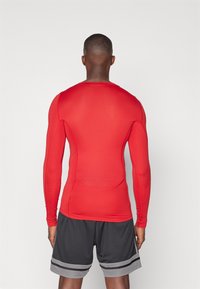 Rød langærmet træningsshirt med en tætsiddende pasform, glat tekstur og rund hals, parret med grå træningsshorts med striber.