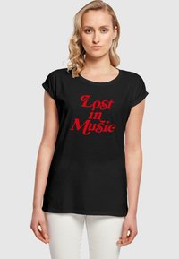Svart kortermet t-skjorte med rund hals som har rød tekst "Lost in Music" i en fet, lekende skrifttype. Glatt stofftekstur.
