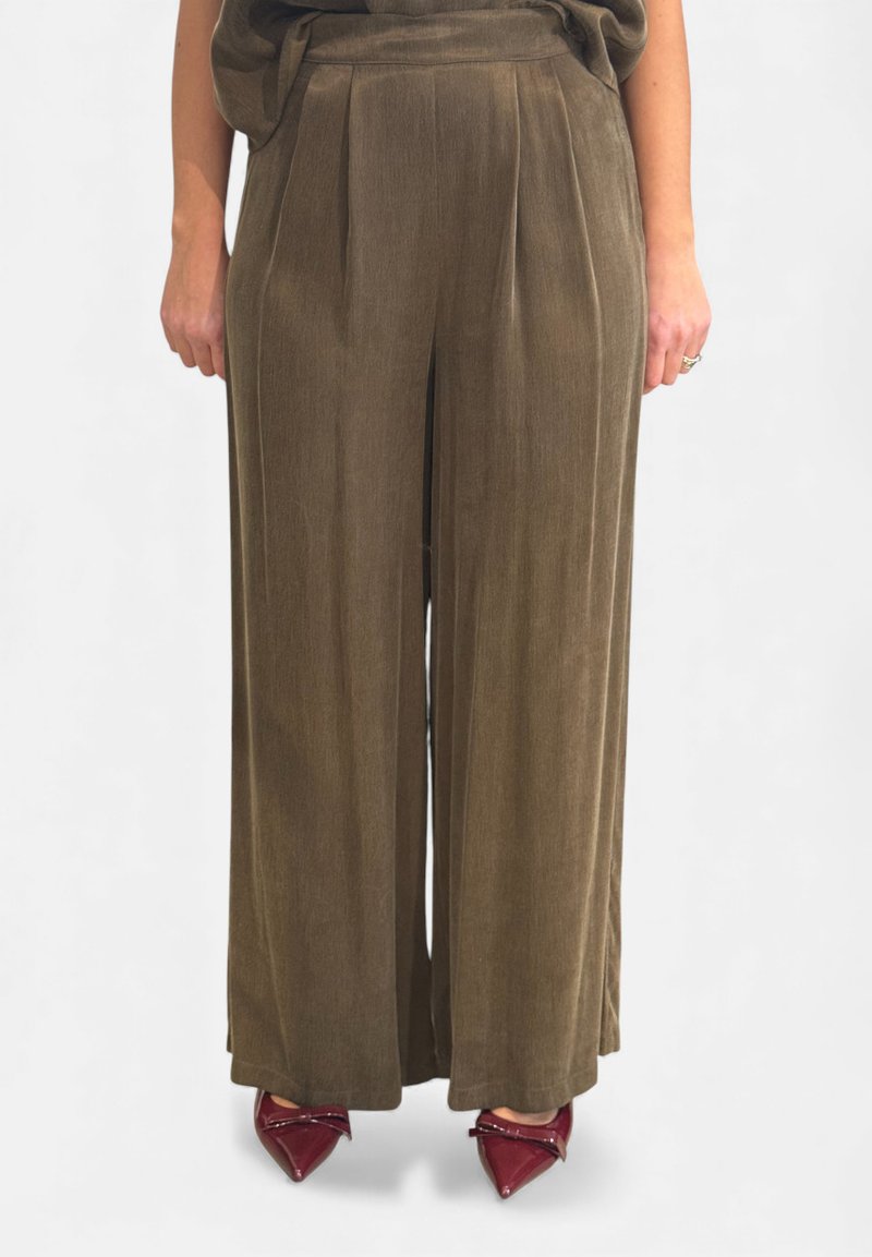 Pantaloni a gamba larga in verde oliva, realizzati in tessuto morbido con finitura strutturata. Presentano pieghe frontali e vita alta, abbinati a tacchi a punta rossi.