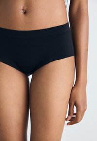Black cotton briefs with a smooth texture, mid-rise waist, and minimalistic design. Close-up view focusing on fit and fabric details.