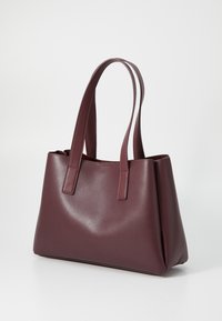 Sac fourre-tout bordeaux en matériau synthétique texturé, avec deux longues poignées et une forme rectangulaire structurée avec des coutures.