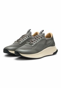Sneakers atletici con superiore in mesh grigio, dotati di sovrapposizioni lisce e di una suola imbottita beige. Inclusi lacci grigi e un tab di estrazione.