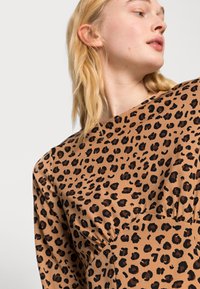 Blusa com padrão de leopardo em tecido bege com manchas pretas. Apresenta um decote redondo e pregas na lateral para adicionar textura e detalhe.