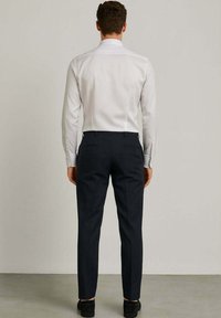 Camicia bianca a maniche lunghe con colletto standard, abbinata a pantaloni blu scuro. I pantaloni hanno due tasche posteriori e una superficie liscia.