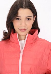 Giacca rosa imbottita con colletto alto e zip rosa. Presenta cuciture a righe orizzontali e una texture leggera e liscia.