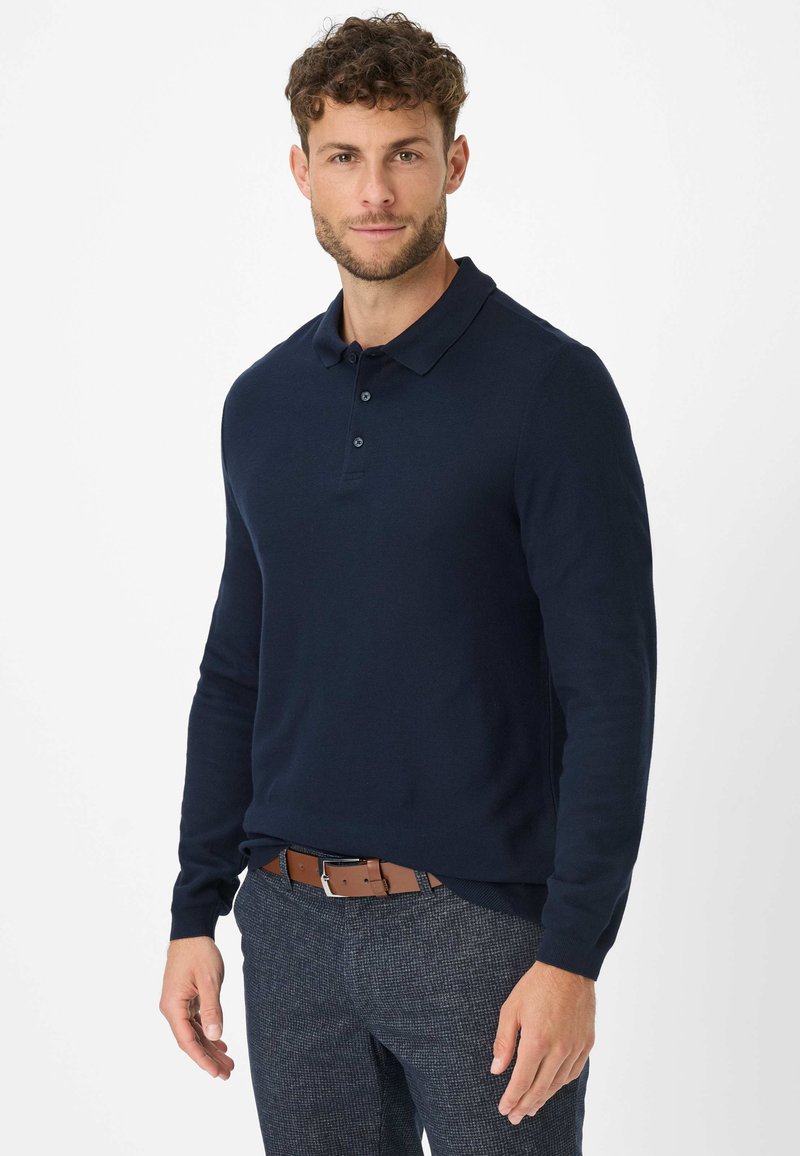 Polo a maniche lunghe blu navy con colletto e pattina a tre bottoni, realizzato in un tessuto liscio, abbinato a pantaloni grigi texturizzati e una cintura marrone.