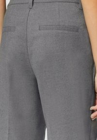 Pantalon gris en tissu texturé avec deux poches arrière et une coupe ajustée. La taille est lisse avec des détails de couture subtils.