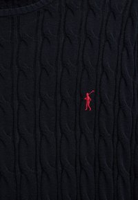 Tessuto azul navy a trecce con una piccola figura rossa ricamata che tiene in mano un mazzuolo da polo al centro a destra.