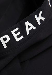 Black sports waistband featuring bold, white “PEAK” lettering, made of elastic fabric with a smooth texture and stitched edges.