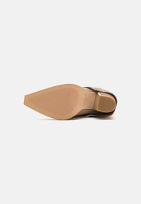 Zapato de ante marrón con punta afilada, que cuenta con una suela de goma texturizada y un tacón bajo y cuadrado. La suela tiene ranuras horizontales para mayor tracción.