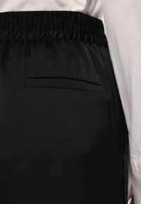 Sort nederdel med elastisk talje og glat tekstur, der har en diskret sidelomme. Stoffet har en blød glans, der fremhæver dets elegante design.