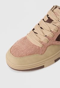 Sneaker in Hellbraun und Hellrosa mit strukturiertem Obermaterial, flachen Schnürsenkeln und Nahtdetails. Verfügt über eine braune Gummisohle und Mesh-Akzente.