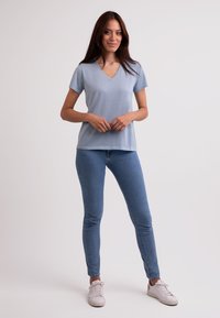 Světle modré tričko s výstřihem do V a krátkými rukávy, zkombinované s modrými skinny džíny a bílými teniskami, vystavené na neutrálním pozadí.