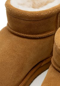 Stivali corti in camoscio color sabbia con un morbido rivestimento interno in pile bianco. Il gambale è cucito con filo a contrasto e presenta una sommità arrotondata.