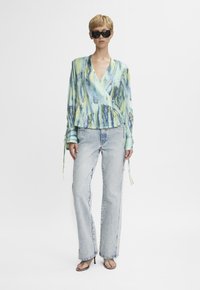 Blusa avvolgente tie-dye azzurro chiaro e verde con maniche lunghe, abbinata a jeans in denim chiaro a vita alta e sandali neri con tacco.
