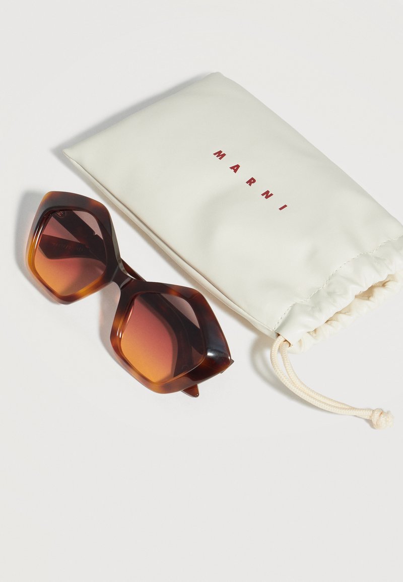 Lunettes de soleil géométriques grandes en écaille avec des verres bruns dégradés à côté d'une pochette blanche à cordon portant l'inscription "Marni".