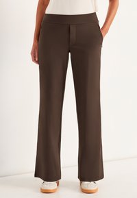 Bruine wijde broek met een zachte textuur, voorzien van een platte tailleband en zijzakken, gecombineerd met witte sneakers.
