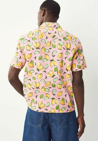 Camisa de manga corta en tejido rosa, con un patrón de limones y limas acompañado de hojas verdes. Diseño con cuello y corte holgado.