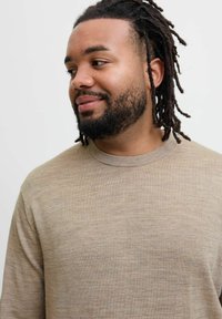 Beige långärmad skjorta med rund halsringning. Mjuk textur med subtila färgvariationer. Modellen har medellånga dreadlocks.