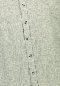 Lichtgroen linnen shirt met een gestructureerde afwerking, voorzien van een voorste knoopsluiting en kleine, donkere knopen.
