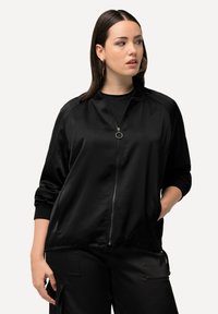 Giacca bomber nera in satin con chiusura frontale a zip, polsini a costine e colletto rotondo. Presenta una texture liscia e tasche laterali.