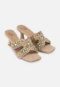 Mule in suede nudo con tacco, dotate di due cinturini incrociati decorati con strass trasparenti e dorati, con punta quadrata e basso tacco a blocco.